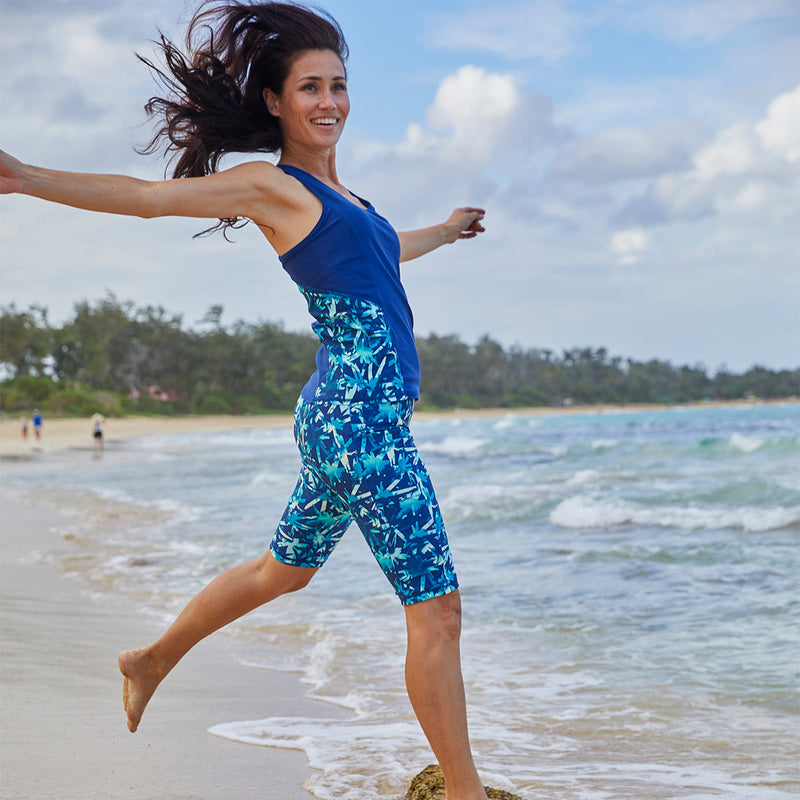 Woman in UV Skinz's women's racerback swim tank top on the beach|tie-dye-burst